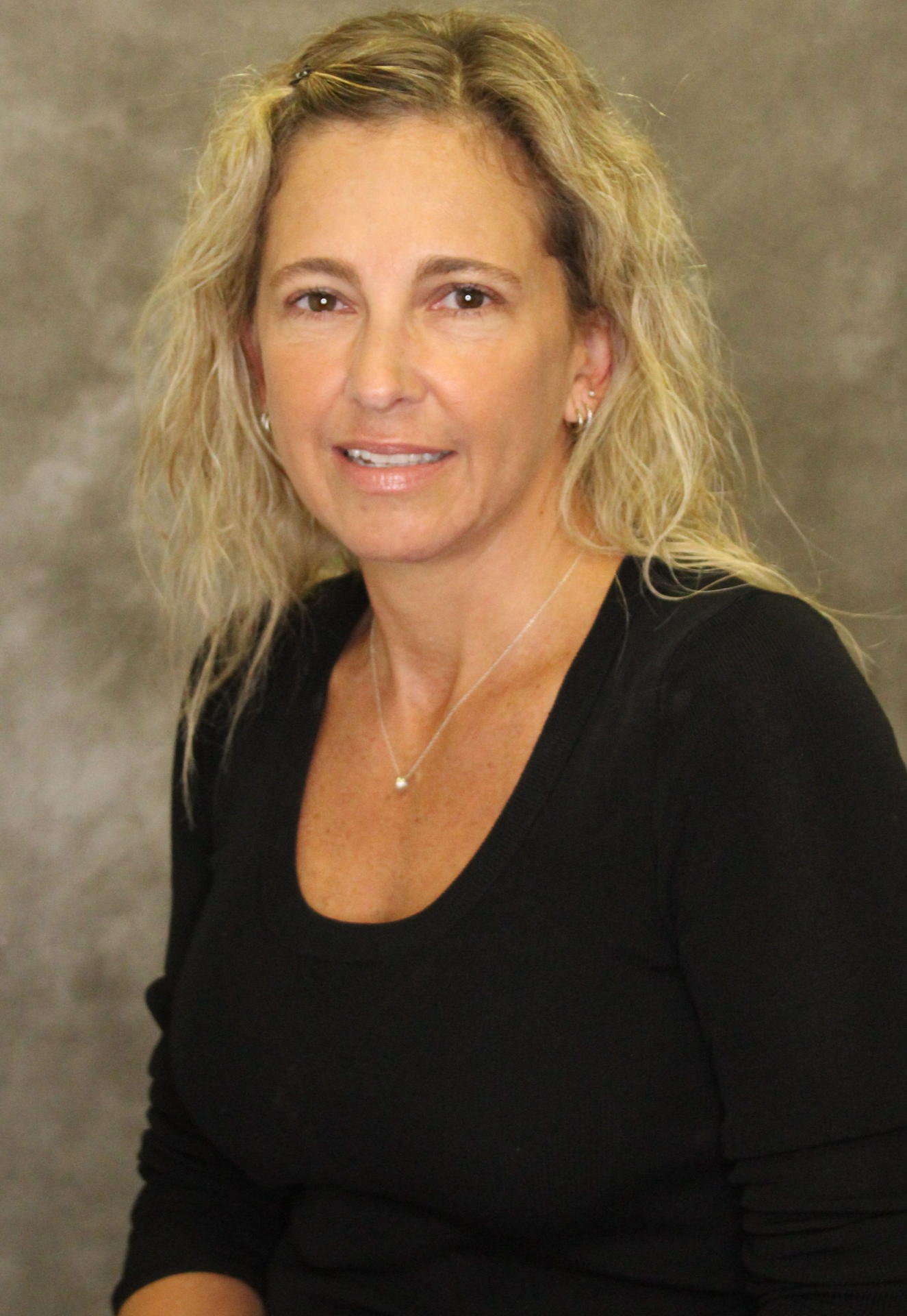 Middle-aged woman with blonde hair wearing a black top against a gray background.