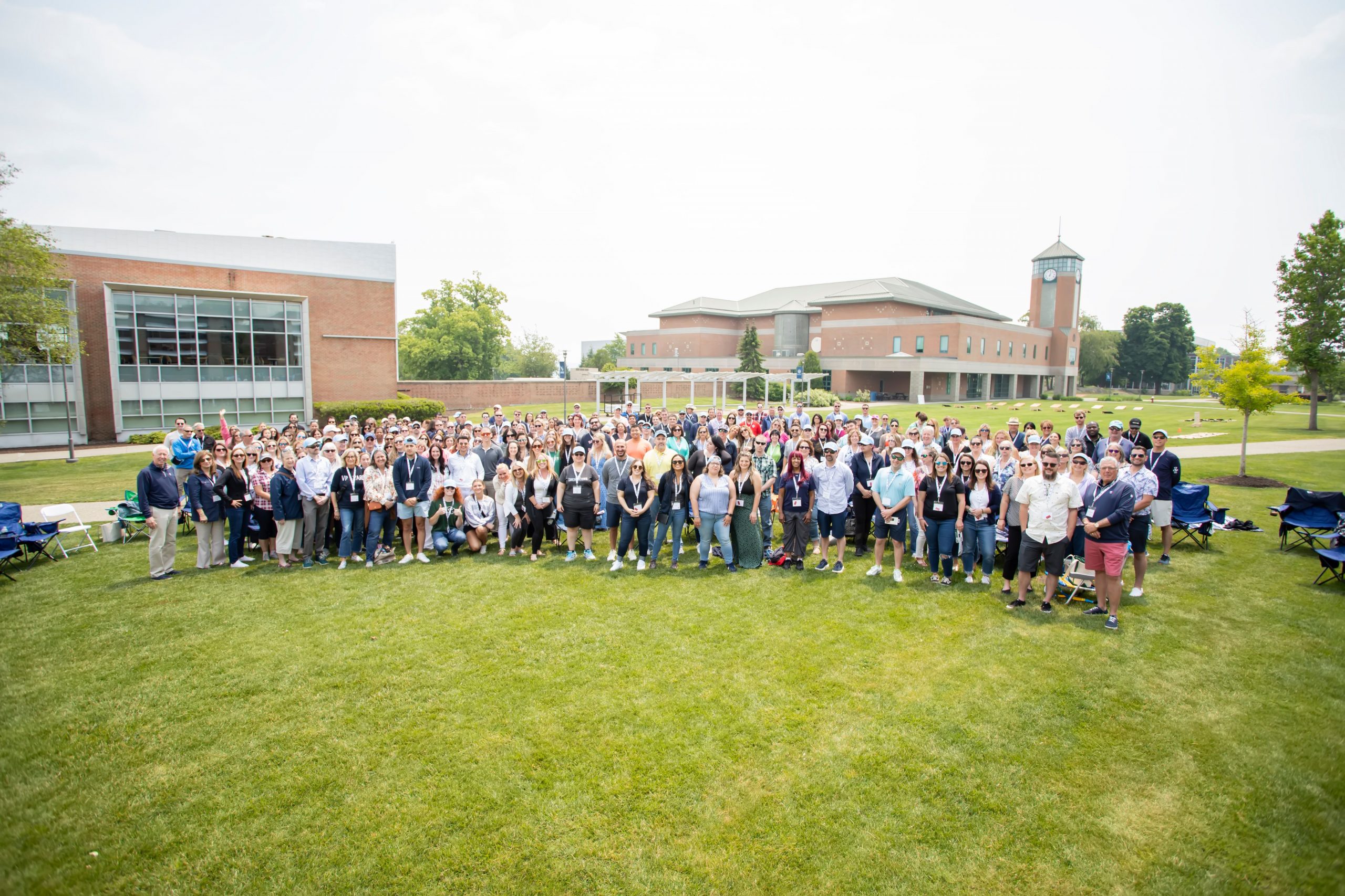 Large group gathering outdoors on a university campus lawn.