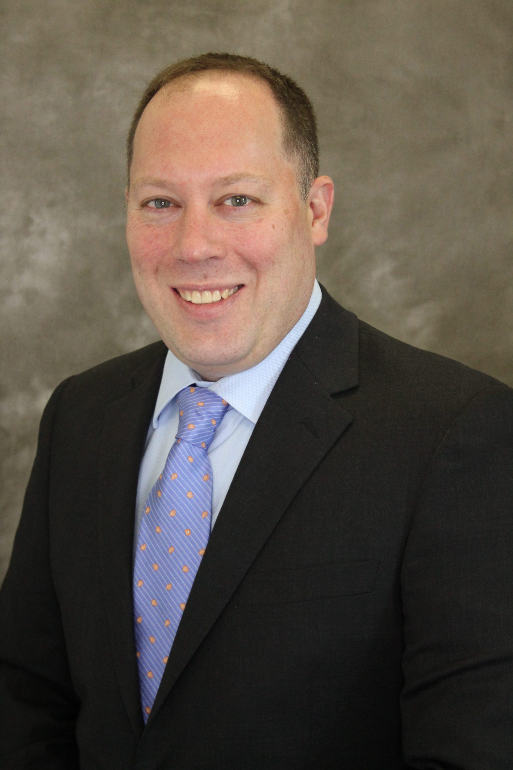 Professional man in business attire smiling against a neutral background.