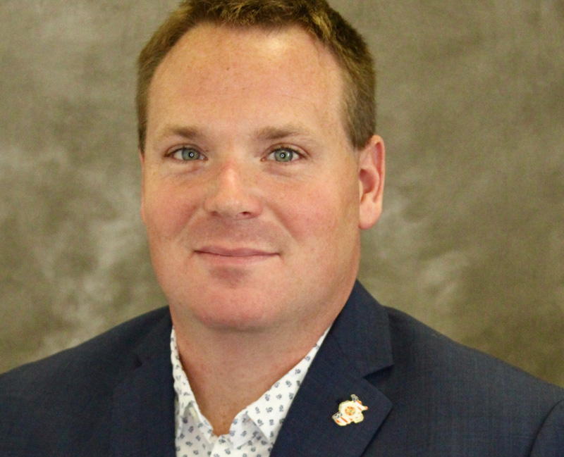 Professional male in suit with decorative lapel pin, neutral background.