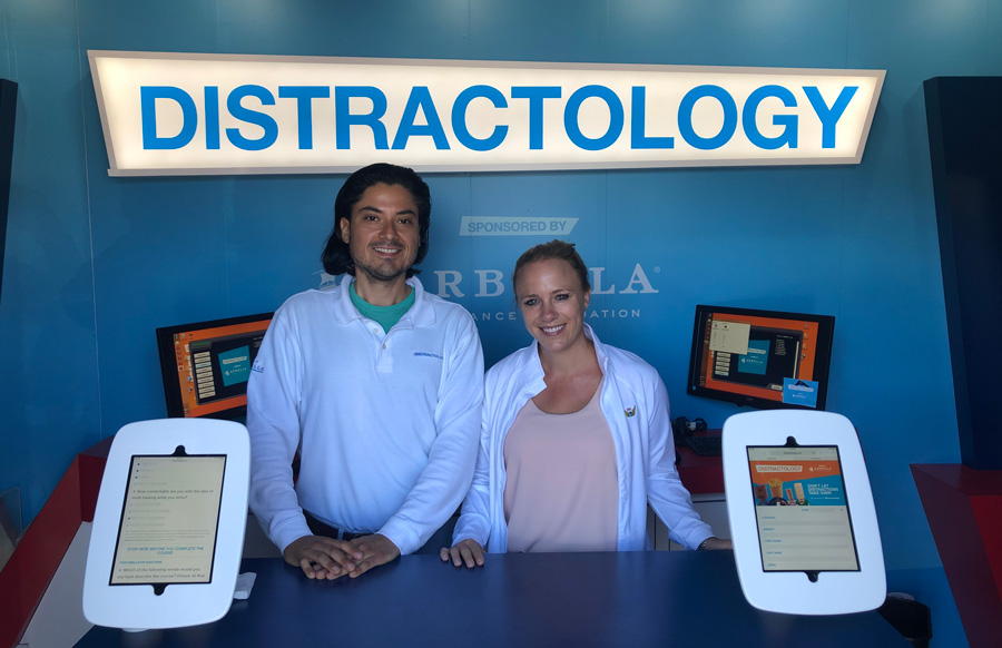 Distractology booth with two people, sponsored by Arbella Insurance Foundation, featuring interactive tablets.