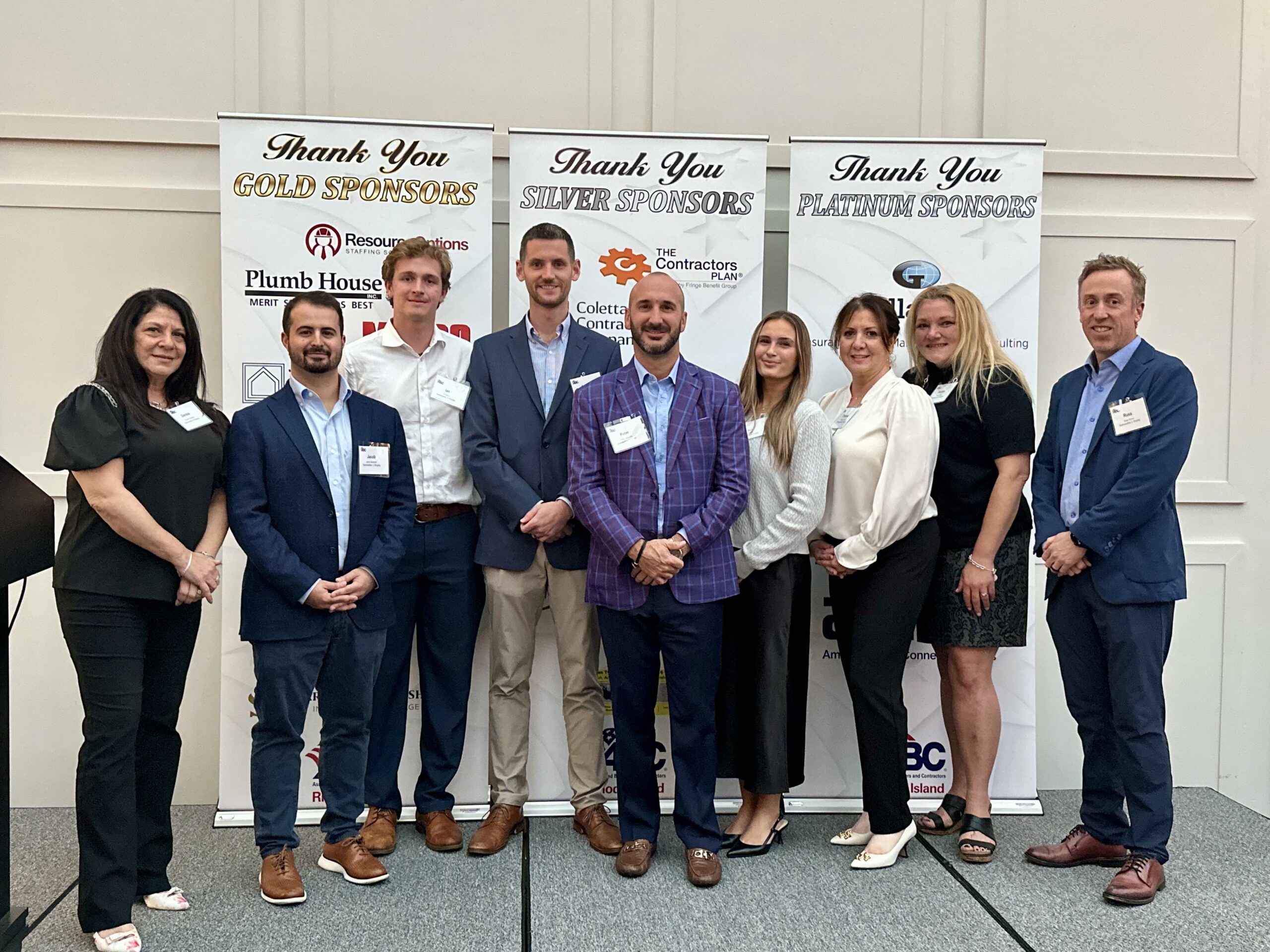 Group of professionals at event with sponsor banners in background.