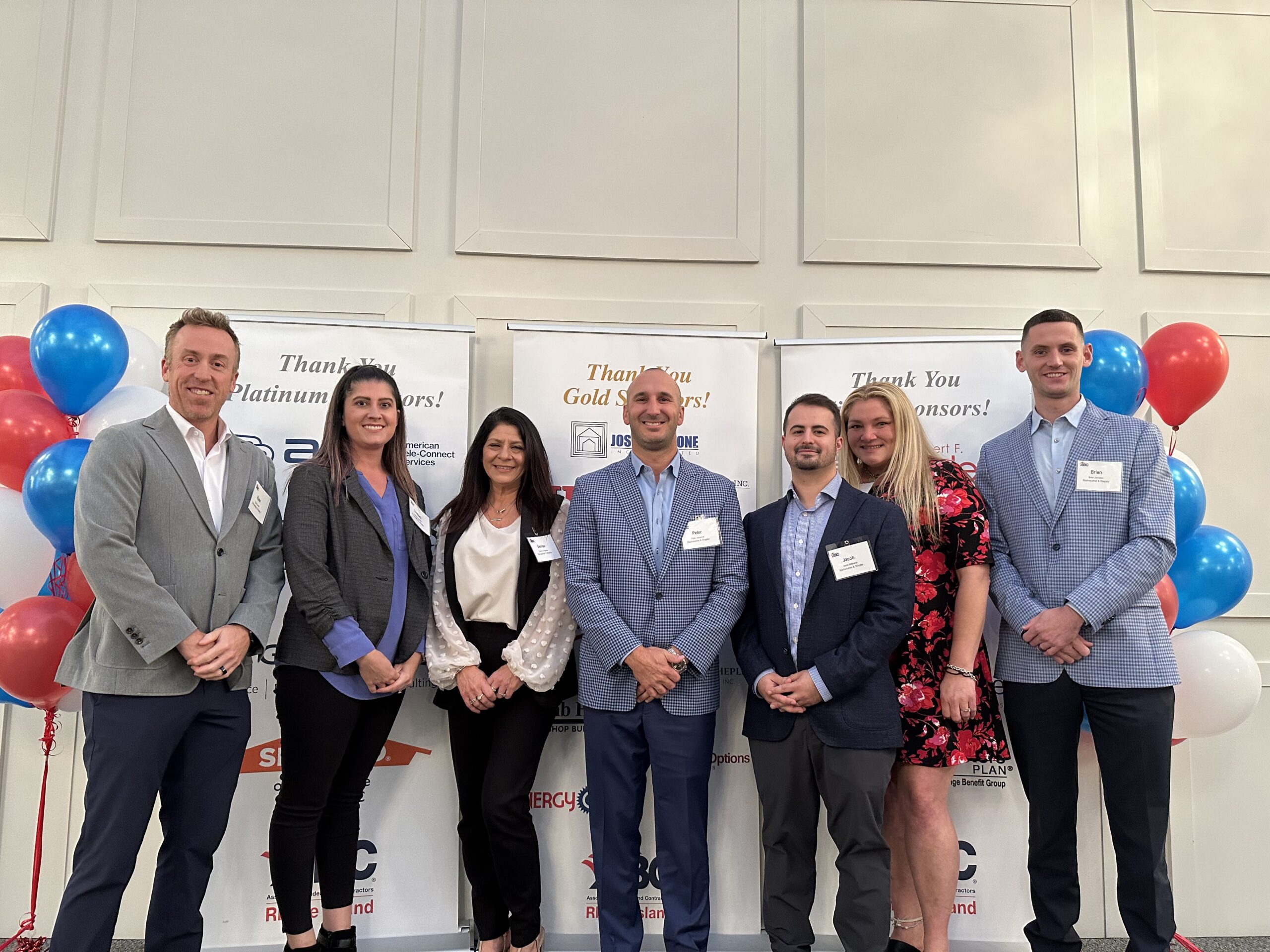 Group of business professionals at a sponsor event with banners and balloons in the background.