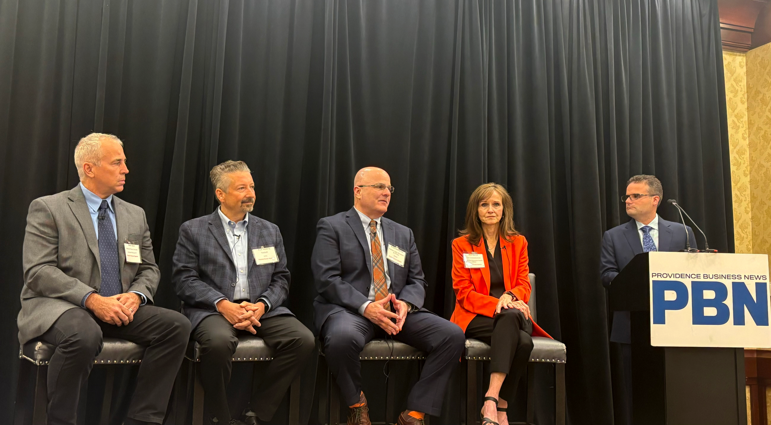Panel discussion at Providence Business News event with five speakers on stage.