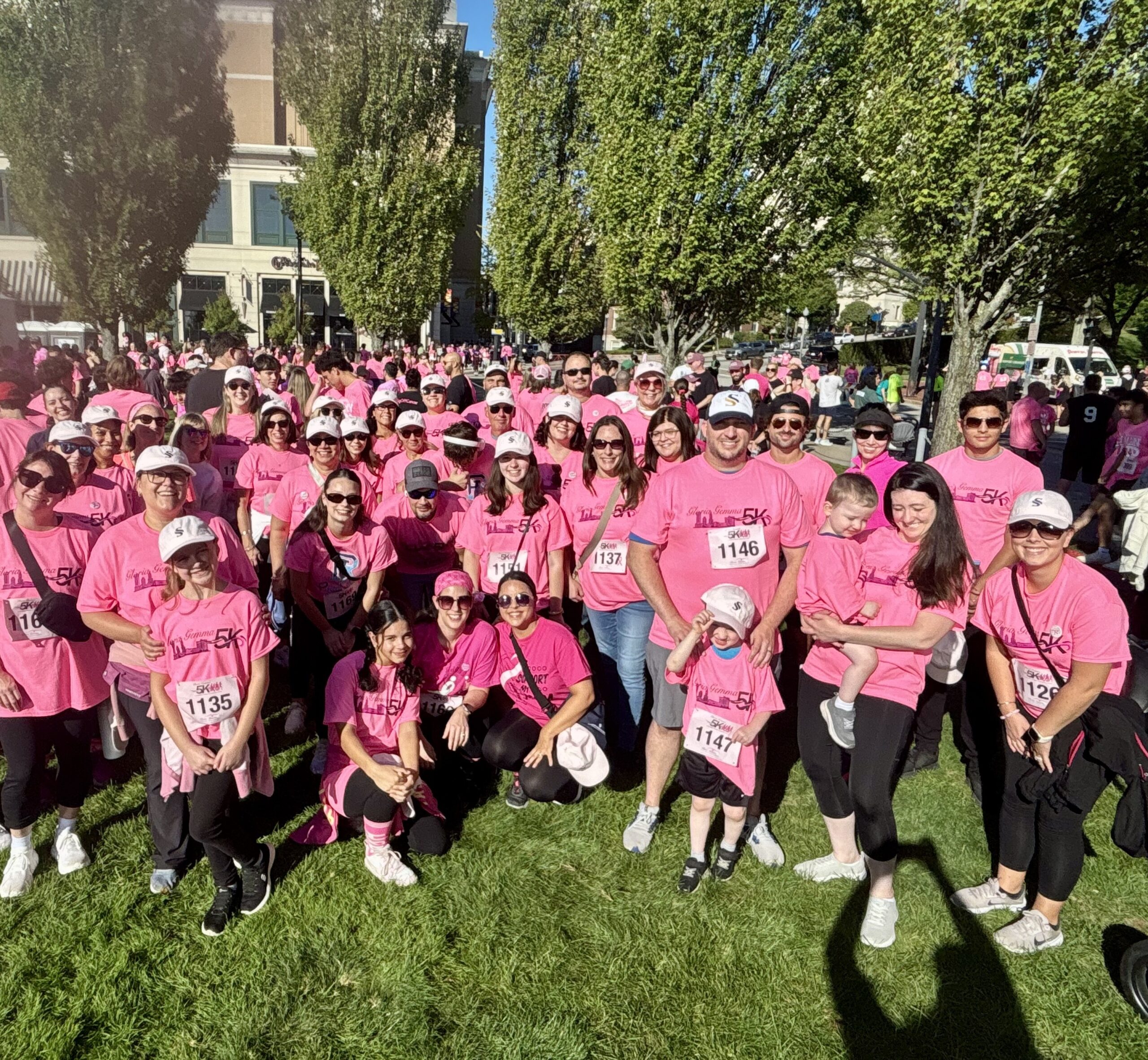 Participants gather in pink shirts for a charity 5K run on a sunny day.