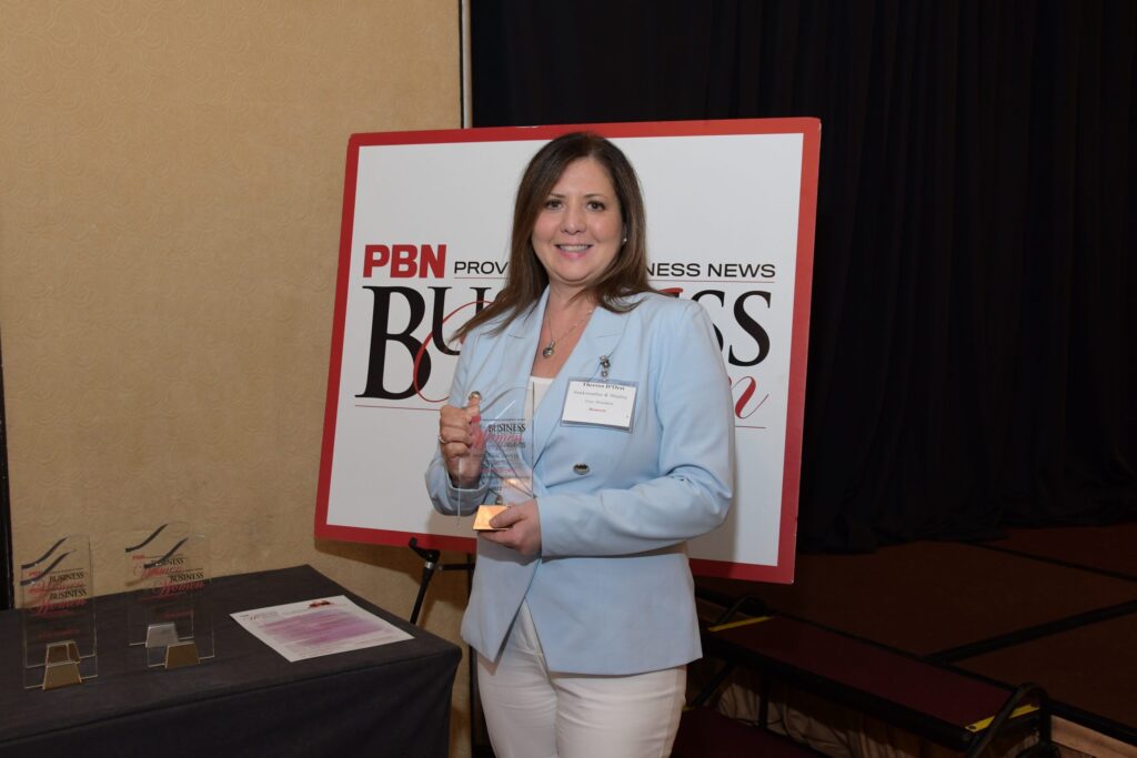 Award recipient at Providence Business News event holding accolade, standing beside PBN signage.