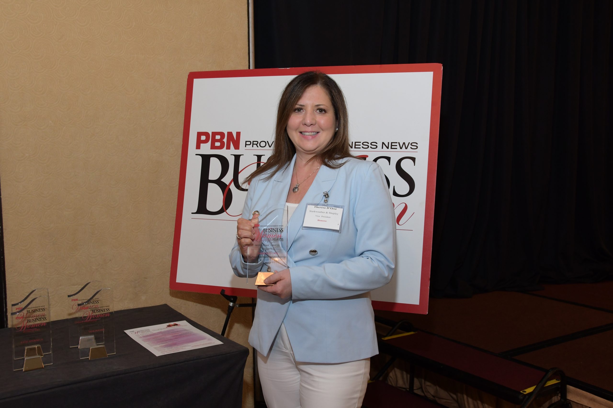 Award recipient at Providence Business News event holding accolade, standing beside PBN signage.
