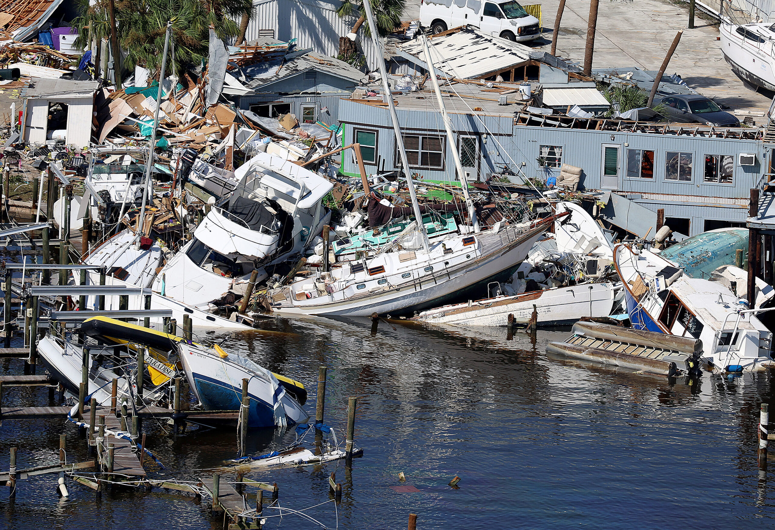 Boats and waterfront property damaged by a hurricane, surrounded by debris and overturned vessels.