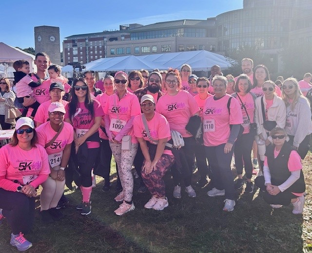 Participants at a 5K event in bright pink shirts gather for a group photo outdoors.