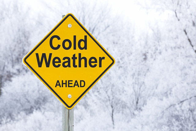 Warning sign reading "Cold Weather Ahead" on snowy background.